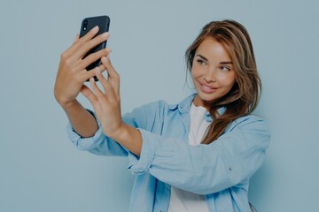 Attractive blogger taking selfie near light blue wall