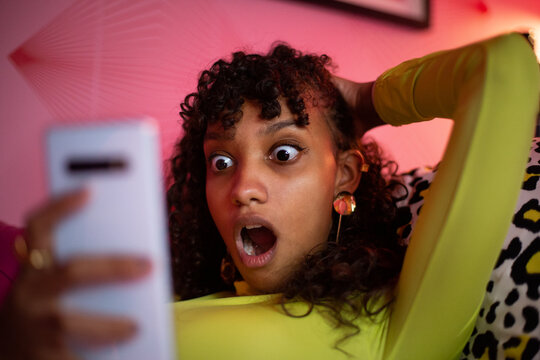 Multiracial young adult female looking shocked at a smartphone