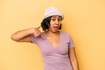 Naklejka premium Young latin woman isolated on yellow background person pointing by hand to a shirt copy space, proud and confident