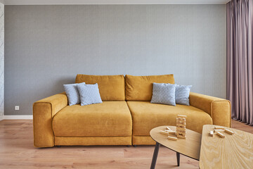A yellow Scandinavian-style sofa with a wooden tower game on the coffee table