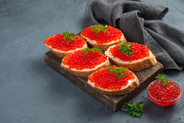 Sandwiches with red caviar butter and fresh parsley on a dark background.