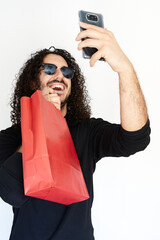 Vertical shot of Black Friday sale concept where young man with sunglasses takes selfie and smiling with red shopping bag