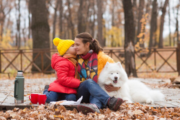 mom and  child daughter walk with a dog and  drinking hot tea from thermos in autumn park.
