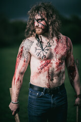 Medieval warrior berserk Viking portrait with tattoo on skin, cuts on body and braids in hair with weapons to attacks enemy. Concept historical photo