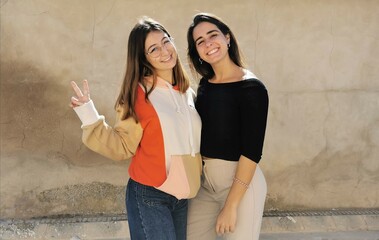 Two beautiful young friends hugging each other making victory sign