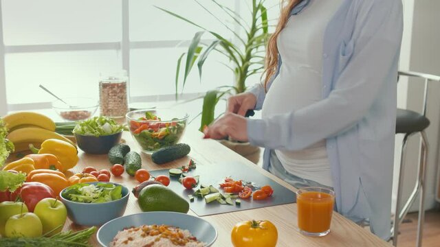 Pregnant Woman in the Kitchen Cuts Tomatoes, Prepares Dinner. Healthy, Organic and Wholesome Food. Vitamins From Fresh Vegetables for the Mother Of ohe Unborn Child. Prepare a Homemade Meal. Close-up.