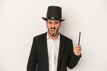 Young magician man holding wand isolated on white background screaming very angry and aggressive.