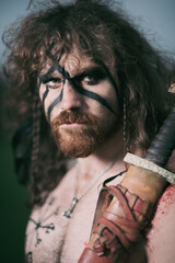 Medieval warrior berserk Viking portrait with tattoo on skin, cuts on body and braids in hair with weapons to attacks enemy. Concept historical photo