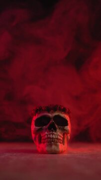 vertical video of halloween skull head with smoke on black background with red orange lights