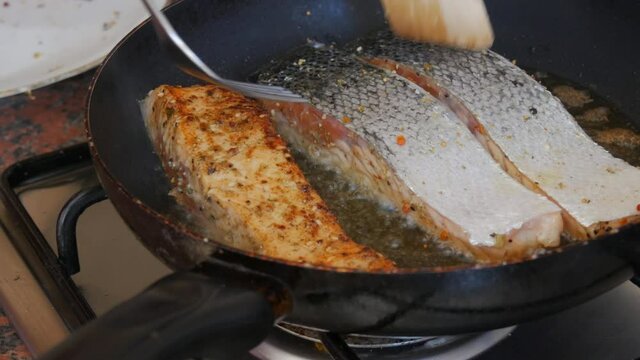 Fillet of red fish salmon salted and seasoned with pepper fried in a frying pan turn over with a wooden kitchen spatula in the home kitchen