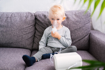 Cute little blond boy does inhalation at home.