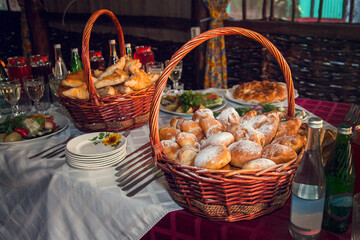 Russian feast. A table set with Russian snacks: stuffed pies pirozhki in large baskets, pickles, drinks poured into glasses - obrazy, fototapety, plakaty