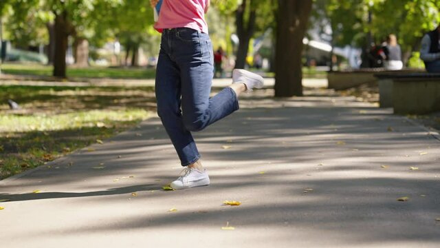 Legs of woman dancing and spinning on walkway in park on sunny day. Partial view of happy person with exercise books in hand. Tracking shot of student after passing exam