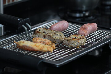 Churrasqueira elétrica com carnes sobre grelha, linguiça, frango e pernil de porco