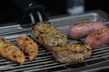 Churrasqueira elétrica com carnes sobre grelha, linguiça, frango e pernil de porco