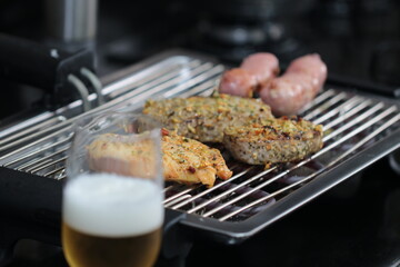 Churrasqueira elétrica com carnes sobre grelha, linguiça, frango e pernil de porco