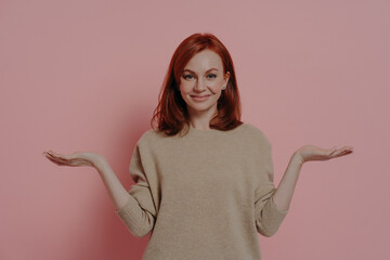 Positive young ginger female comparing two variants options, isolated on pink background