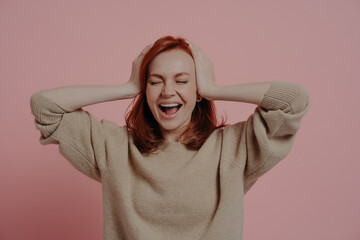 Excited caucasian red-haired woman reacting positively on good news isolated over pink background