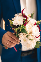 groom in a blue suit holds a wedding bouquet
