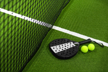 Closeup view of a paddle racket and balls in a padel tennis court near the net. Green background...