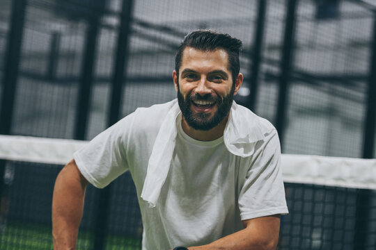 Beautiful man playing paddle tennis, racket in hand smiling after a win. Young sporty boy at the end of the match. Sweaty padel athlete ready to take shower. Sport, health, youth and leisure concept