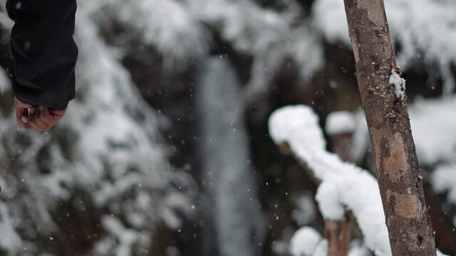 Slow motion shot of snowfall with man in the background walking towards the Jana waterfall at Kullu in Himachal Pradesh, India