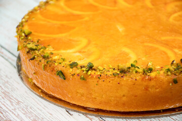 Delicious sweet orange cake decorated with orange slices, orange jam and pistachio nuts on the table. Celebration