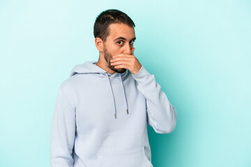 Young caucasian man isolated on blue background covering mouth with hands looking worried.