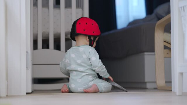 Cute baby boy wearing soft safety helmet discovering new things at home, 7 month old infant on the floor playing, learning to walk, craw sit and stand. High quality 4k footage