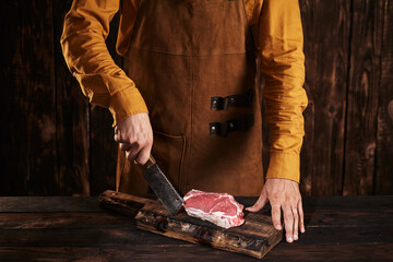 Butcher with a knife in a leather apron. Raw meat on a wooden board.