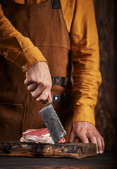 Butcher with a knife in a leather apron. Raw meat on a wooden board.