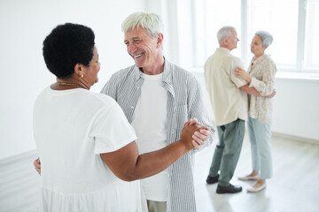 Obraz premium Two senior couples smiling to each other holding hands while dancing a slow dance in dance studio