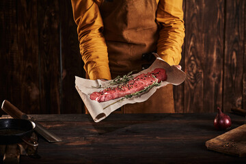 A man in an apron holds a large piece of meat on paper.