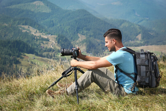 Man taking photo of mountain landscape with modern camera on tripod outdoors