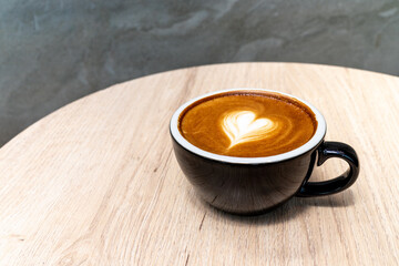 Latte coffee or cappuccino coffee in black cup with beautiful heart latte art on wooden table.