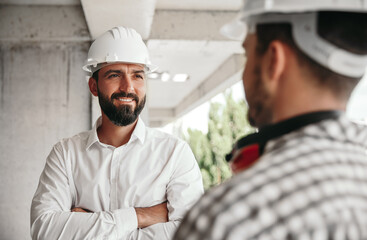 Smiling foreman and builder in hardhats at construction site