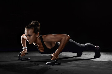 Fototapeta na wymiar Female athletes with holders doing push-ups in gym in darkness