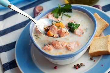 Creamy salmon soup Kalakeitto with salmon, carrot, parsley, onion, garlic, potatoes, croutons and spoon on white background. Spoon of traditional Finnish hot soup. 