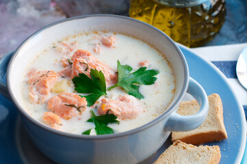 Creamy salmon soup Kalakeitto with salmon, carrot, parsley, onion, garlic, potatoes, croutons and spoon in blue bowl. Traditional Finnish hot soup