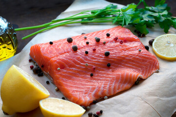 Trout fillet with lemon, parsley, allspice, olive oil on parchment paper on dark brown background