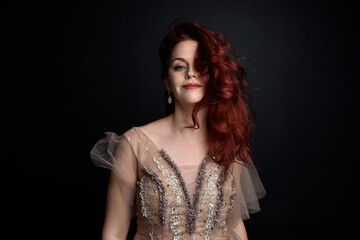 close up portrait of red haired  girl wearing a creamy fantasy gown like a fairy goddess costume.  isolated on dark studio background.
