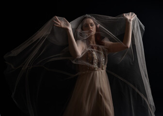 Naklejka premium Full length portrait of red haired girl wearing a creamy fantasy gown like a fairy goddess costume. standing pose with elegant gestural movement , isolated on dark studio background.