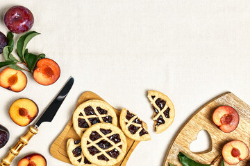 Mini homemade plum tarts with fresh sliced plum fruits on wooden plate top view. Delicious plum quiche on the table with linen tablecloth view from above with space for text.