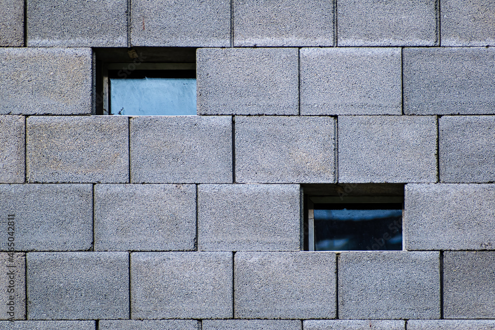 Poster two different small square windows on the outer wall of a cement block
