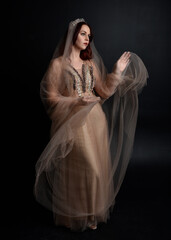 Full length  portrait of red haired  girl wearing a creamy fantasy gown like a fairy goddess costume.  standing  pose with elegant gestural movement , isolated on dark studio background.