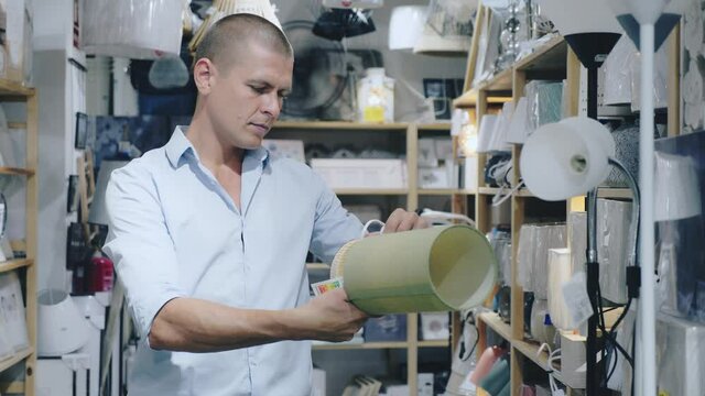 Man standing in store and choosing table lamps. He's holding one in hands and looking at it.