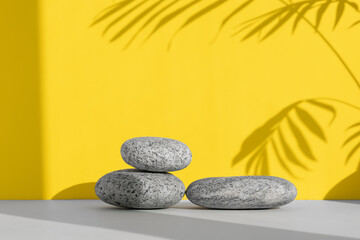 Fototapeta na wymiar Podiums made of stones on a gray table on a yellow background with a shadow from the leaves of a palm tree. Showcase for product promotion, beauty, natural eco cosmetic.