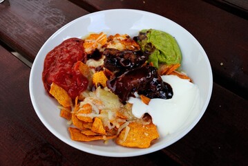 Loaded Nachos made of tortilla chips, Nacho cheese sauce, Cheddar, salsa, sour cream, guacamole, red chili, spring onion, coriander and Pulled Pork in Salisbury, UK