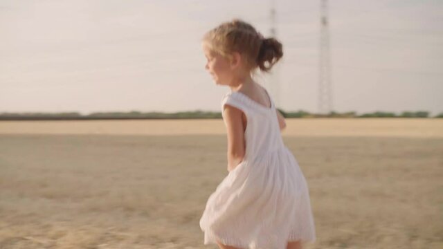 Little girl running sunny day agricultural field dressed white dress Happy childhood concept Cute caucasian female child run on field slow motion Freedom purity Handheld effect Active leisure