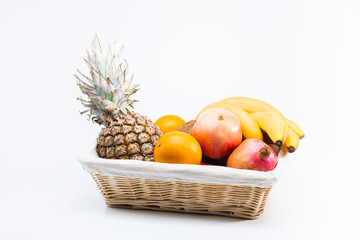 Set of fresh fruits in the basket on a white surface. Balanced diet: pineapple, oranges, pomegranates, apples, bananas, coconuts	